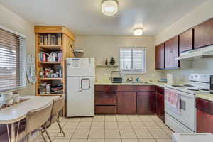 Kitchen featuring open shelves, light countertops, a sink, white appliances, and under cabinet range hood