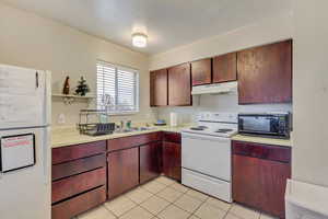 Kitchen featuring white appliances, light countertops, under cabinet range hood, a sink, and light tile patterned flooring