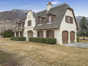 French country style house with a mountain view, a chimney, stucco siding, a front lawn, and driveway