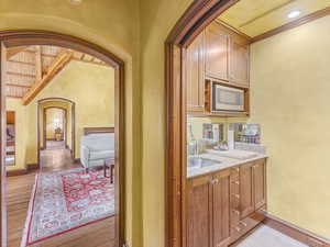 Bar with arched walkways, light stone counters, brown cabinets, stainless steel microwave, and light wood finished floors
