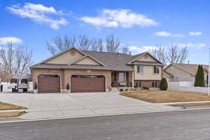 Tri-level home featuring brick siding, stucco siding, fence, a garage, and driveway