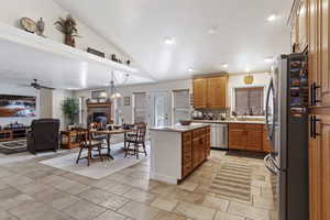 Kitchen featuring a fireplace, light countertops, appliances with stainless steel finishes, open floor plan, and vaulted ceiling