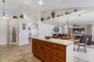 Kitchen featuring arched walkways, open floor plan, light countertops, brown cabinets, and pendant lighting