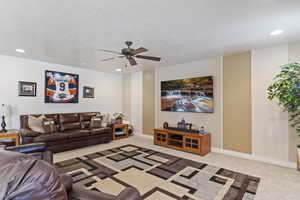 Living room with baseboards, light colored carpet, ceiling fan, a textured ceiling, and recessed lighting