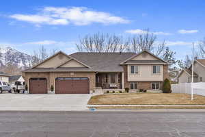 View of front facade with a garage, a shingled roof, concrete driveway, fence, and brick siding