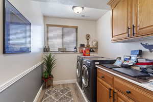 Laundry area with washer and clothes dryer, light wood finished floors, visible vents, cabinet space, and baseboards