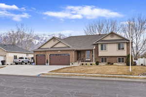 Tri-level home with driveway, brick siding, roof with shingles, an attached garage, and stucco siding