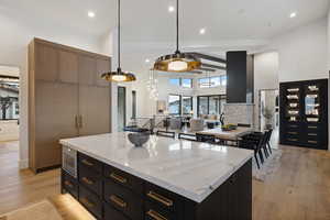 Kitchen featuring a center island, a towering ceiling, light stone countertops, and light wood-style floors