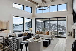 Living room featuring an inviting chandelier, a high ceiling, light wood-style floors, a fireplace, and beam ceiling