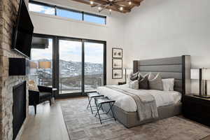 Bedroom with beamed ceiling, access to outside, a stone fireplace, light wood-type flooring, and a notable chandelier