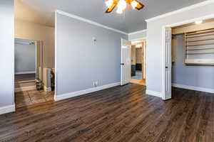 Unfurnished bedroom featuring dark wood-style floors, ornamental molding, a ceiling fan, and baseboards