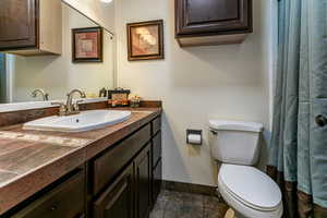 Bathroom with baseboards, toilet, curtained shower, stone finish flooring, and vanity