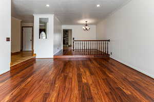 Empty room featuring baseboards, crown molding, wood finished floors, and a notable chandelier