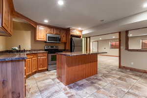 Kitchen featuring stainless steel appliances, dark countertops, recessed lighting, a kitchen island, and a sink