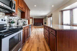 Kitchen with stainless steel appliances, a sink, backsplash, light wood finished floors, and crown molding