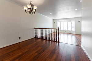 Empty room featuring ornamental molding, baseboards, a notable chandelier, and hardwood / wood-style floors