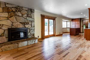 Living area with baseboards, light wood-style flooring, ornamental molding, a stone fireplace, and recessed lighting