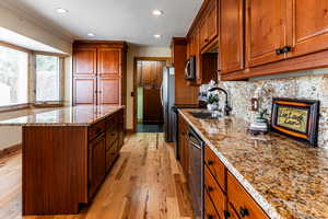 Kitchen featuring stainless steel appliances, a sink, a center island, decorative backsplash, and light wood finished floors