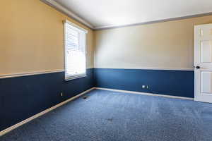 Carpeted empty room featuring a wainscoted wall, visible vents, and crown molding