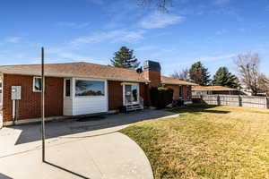 Rear view of house featuring entry steps, brick siding, fence, a lawn, and a chimney