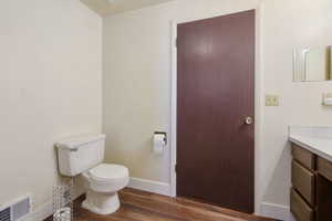 Bathroom featuring toilet, wood finished floors, vanity, visible vents, and baseboards