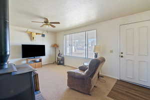 Carpeted living room featuring a textured ceiling, ceiling fan, a wood stove, and baseboards