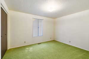 Empty room with baseboards, carpet, visible vents, and a textured ceiling