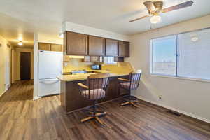 Kitchen featuring visible vents, dark wood finished floors, freestanding refrigerator, a peninsula, and light countertops