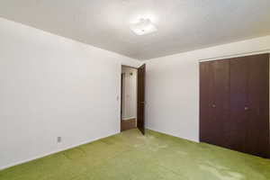 Unfurnished bedroom with light carpet, a closet, a textured ceiling, and baseboards