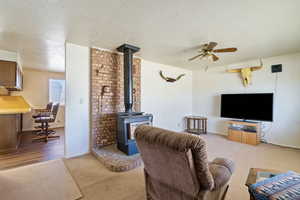 Living room with a textured ceiling, carpet flooring, a ceiling fan, baseboards, and a wood stove