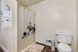 Bathroom with toilet, a shower with shower curtain, wood finished floors, visible vents, and baseboards