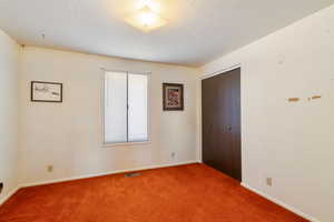 Unfurnished bedroom featuring carpet floors, a closet, visible vents, and a textured ceiling