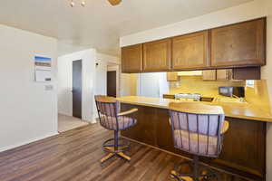 Kitchen featuring a breakfast bar, light countertops, under cabinet range hood, and white gas range oven