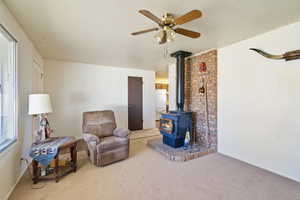 Living area featuring a textured ceiling, ceiling fan, carpet flooring, and a wood stove