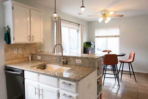 Kitchen with tasteful backsplash, white cabinets, dishwashing machine, a peninsula, and a sink