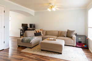 Living area featuring arched walkways, crown molding, baseboards, and wood finished floors