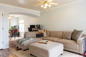 Living area featuring arched walkways, ceiling fan, wood finished floors, baseboards, and crown molding