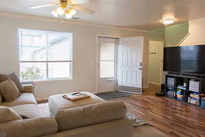 Living area with a ceiling fan, crown molding, visible vents, and wood finished floors