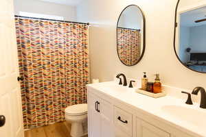 Bathroom with double vanity, a sink, toilet, and wood finished floors