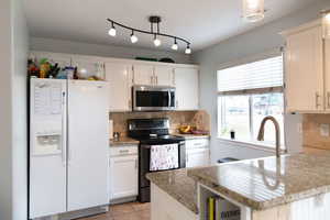 Kitchen with stainless steel appliances, white cabinetry, backsplash, and light tile patterned floors