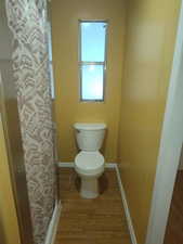 Bathroom featuring curtained shower, baseboards, toilet, and wood finished floors