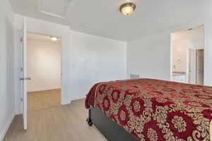 Bedroom featuring baseboards, light wood finished floors, visible vents, and attic access