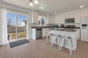 Kitchen with dark countertops, light wood-type flooring, appliances with stainless steel finishes, and white cabinets