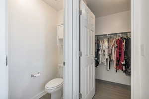 Bathroom with baseboards, a spacious closet, toilet, and wood finished floors