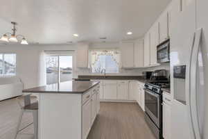 Kitchen with light wood finished floors, stainless steel appliances, dark countertops, white cabinetry, and a kitchen island