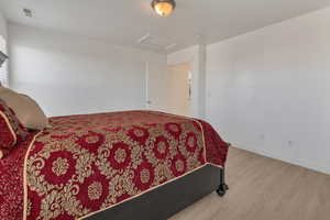 Bedroom featuring attic access, visible vents, baseboards, and wood finished floors