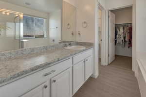 Bathroom featuring a shower with shower door, wood finished floors, vanity, baseboards, and a walk in closet