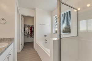 Full bath featuring a walk in closet, a garden tub, vanity, a shower stall, and wood finished floors