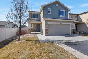 View of front of house with driveway, stone siding, roof mounted solar panels, and fence