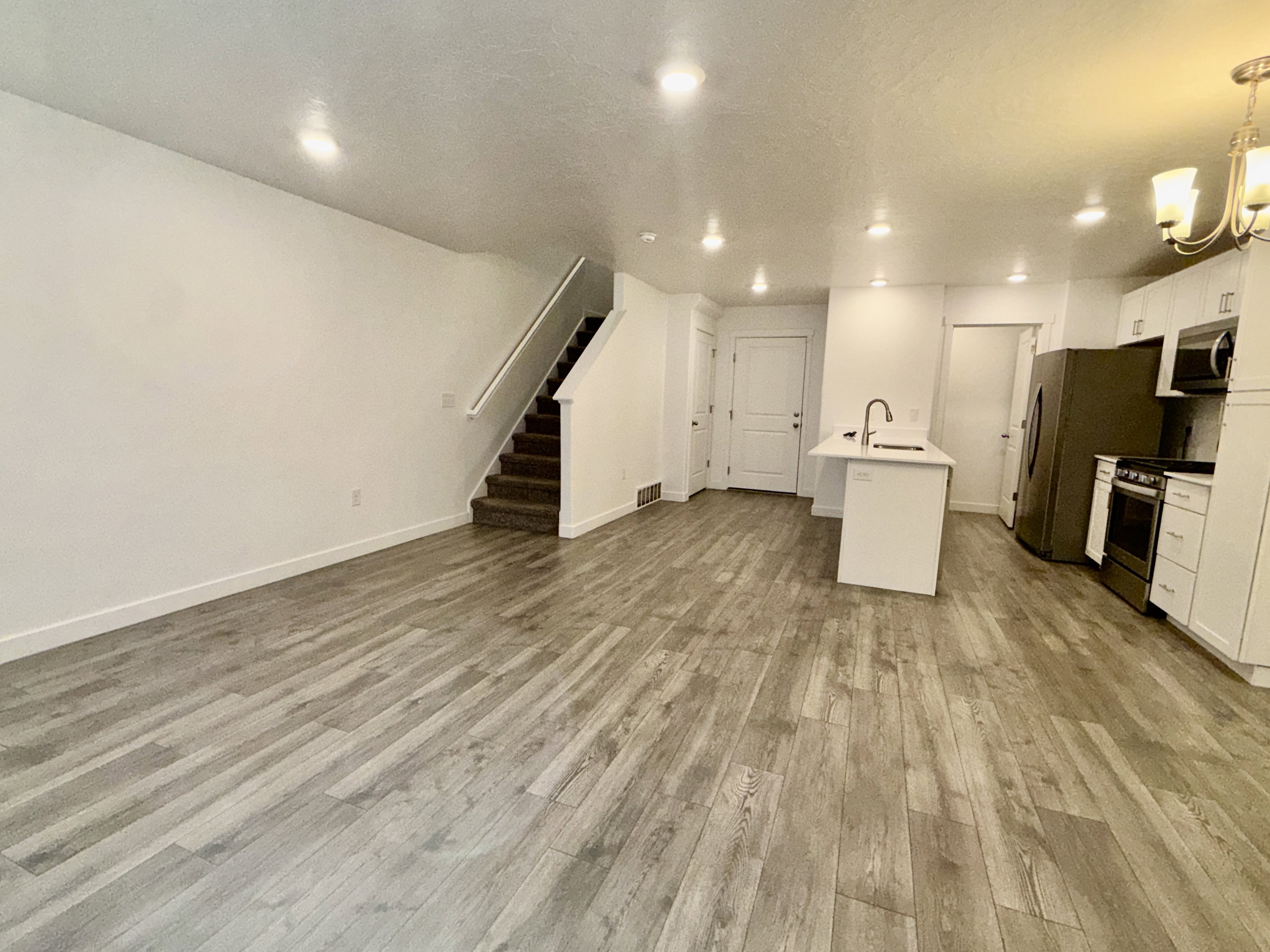 Open-concept living space featuring wood-finish flooring, recessed lighting, and a white kitchen with stainless steel appliances